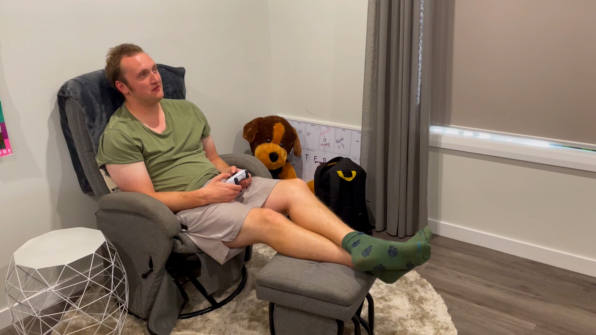 Man in green shirt playing video games in his bedroom. Modern Orana SIL home in Loxton, South Australia Bedroom with private ensuite in Loxton NDIS supported independent living home Shared BBQ area and paved seating at Loxton SIL homes