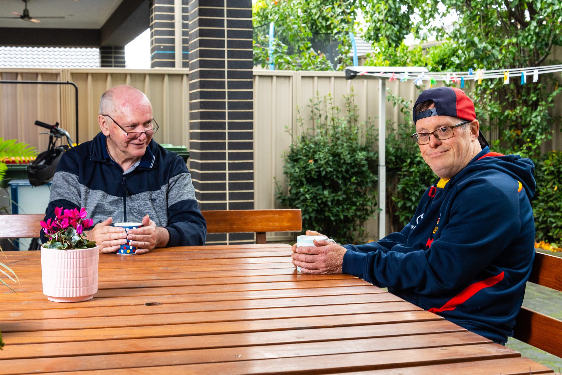 two men sitting at a table having a cup of tea.
