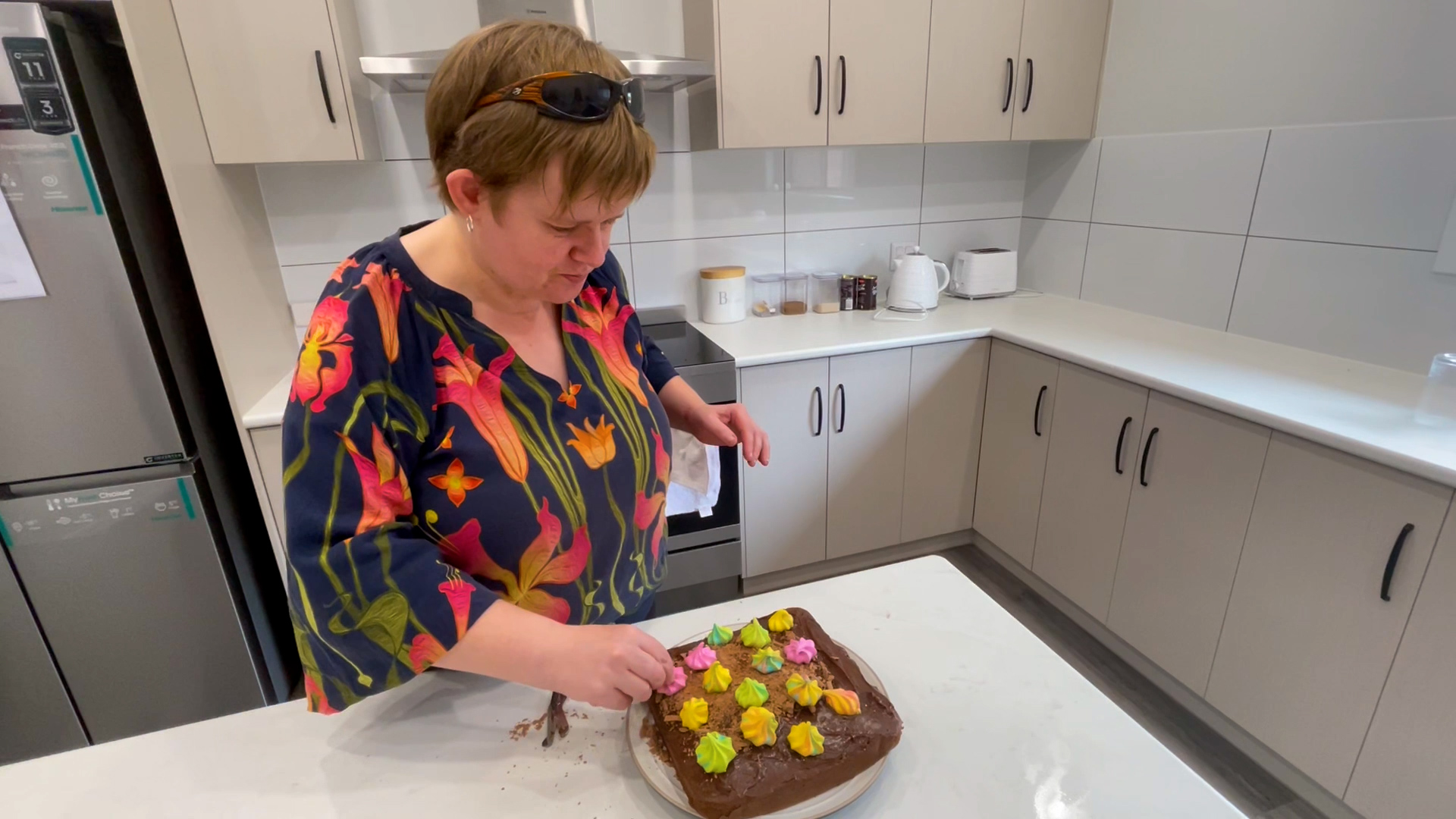 Woman in floral top placing colourful decorations on a cake. Modern Orana SIL home in Loxton, South Australia Bedroom with private ensuite in Loxton NDIS supported independent living home Shared BBQ area and paved seating at Loxton SIL homes