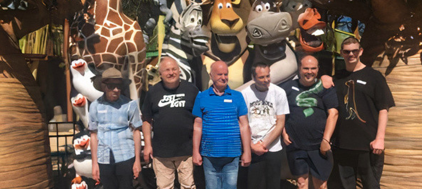 Six male clients standing in the sun in front of the main character from DreamWorks Magagascar movie.