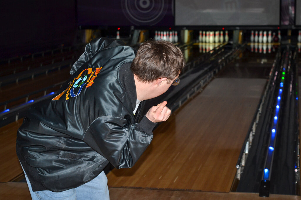 Man in black jacket bowling a ball down a bowling alley