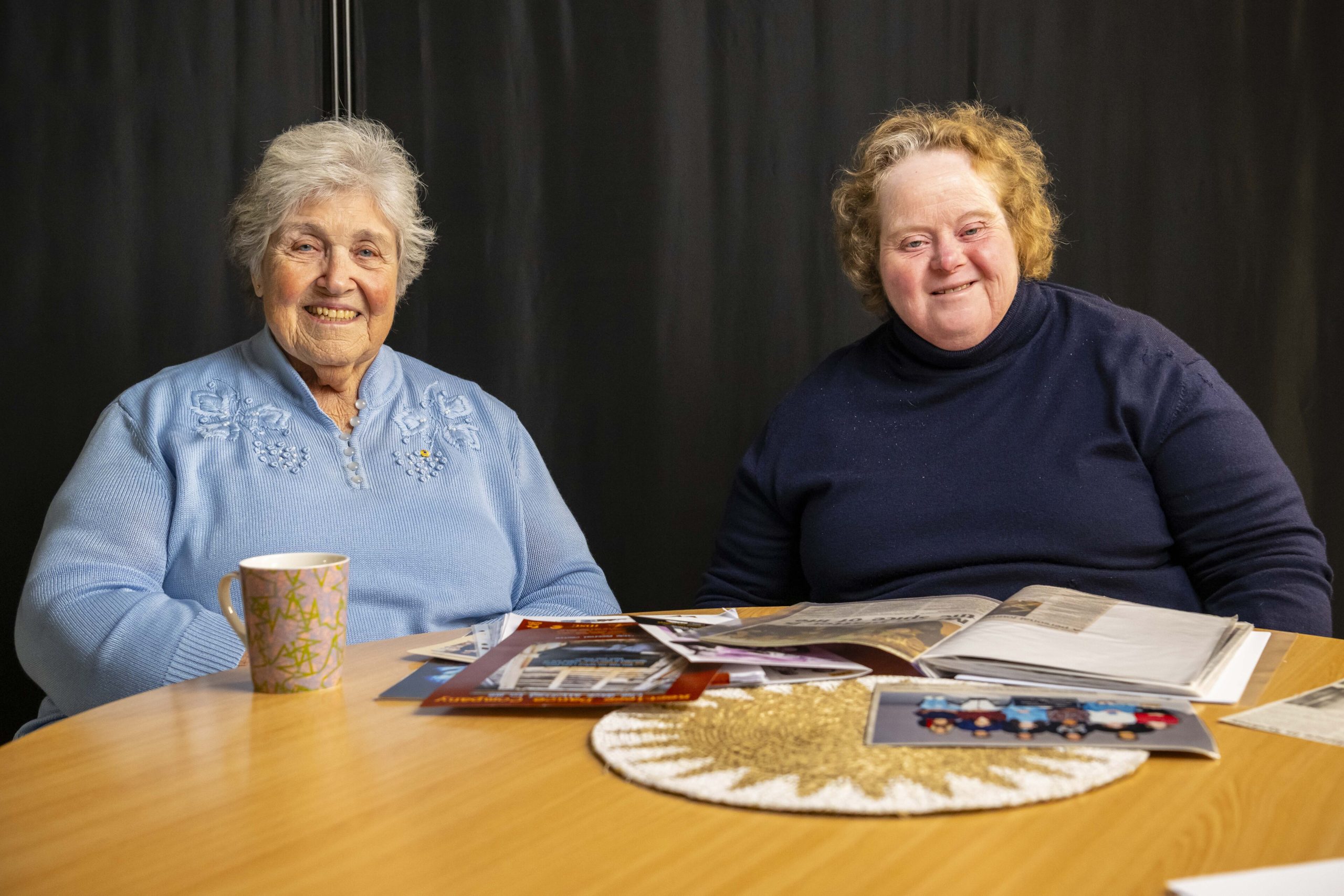 Woman and daughter sit at a table covered with family photos smiling for the camera