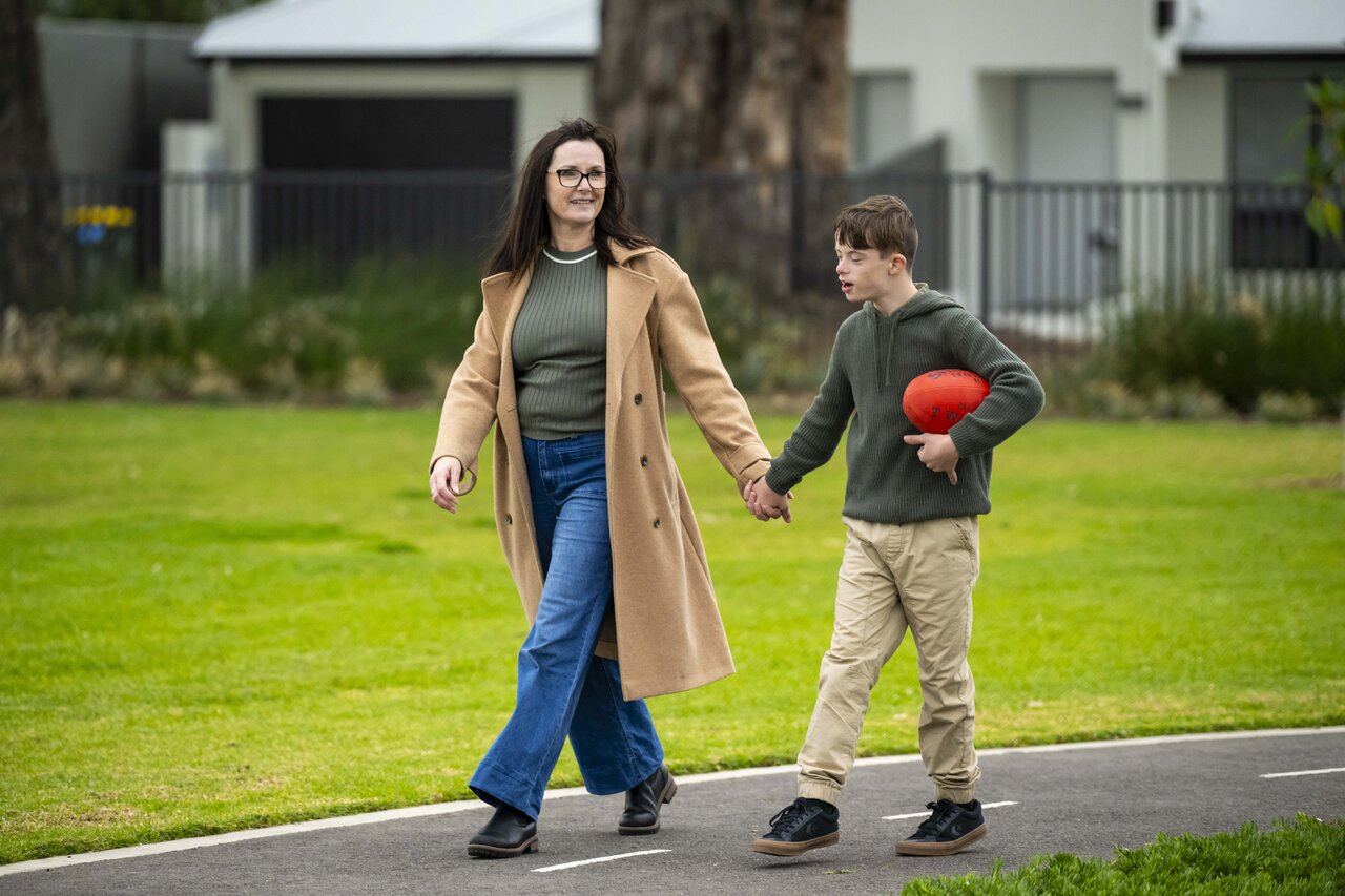 Mother in and son walk hand in hand in a park while son holds a football