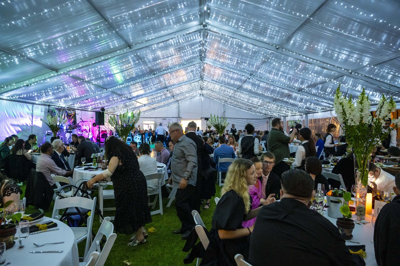 Inside a large tent at a gala filled with people and fairy lights across the ceiling