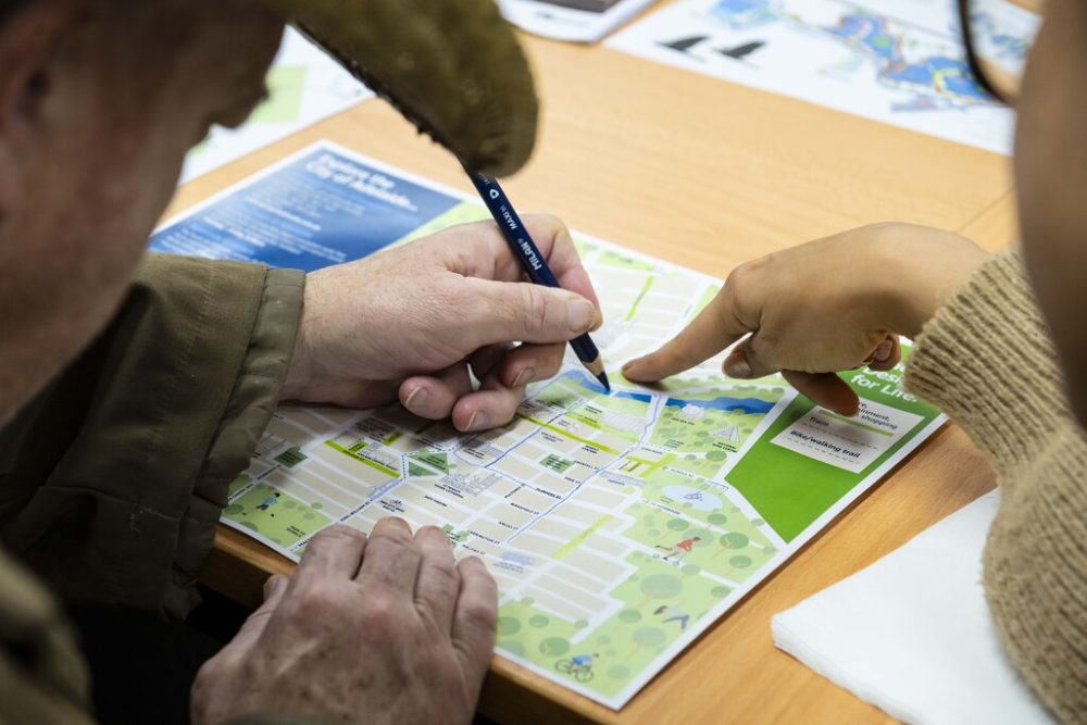 Two hands pointing at a map, one with a pencil in their hand