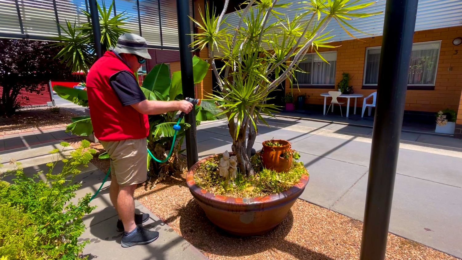 Man watering plants as part of disability support services in Adelaide, promoting independence and community inclusion.