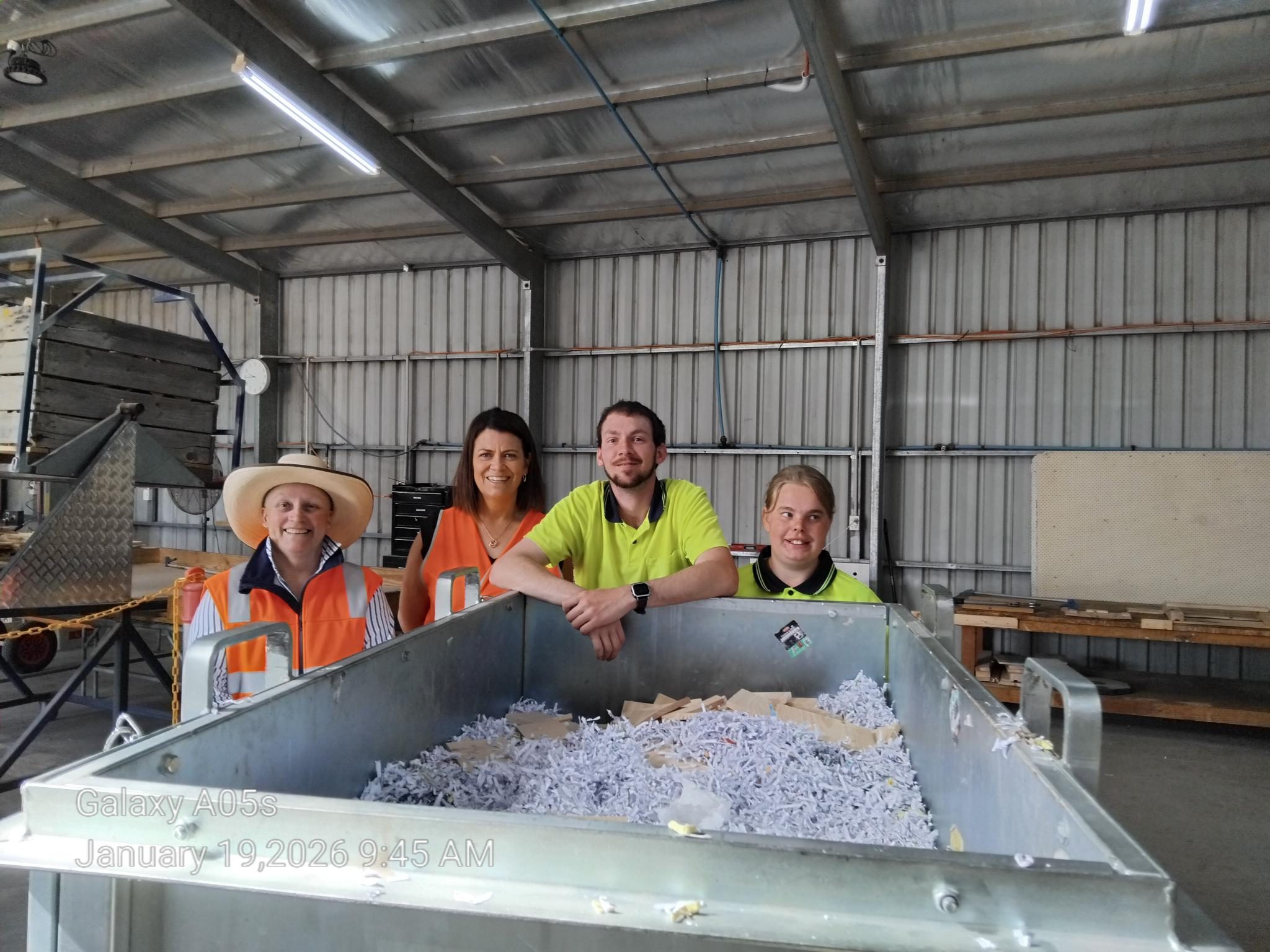 Four people in hi-vis smile for the camera in a warehouse
