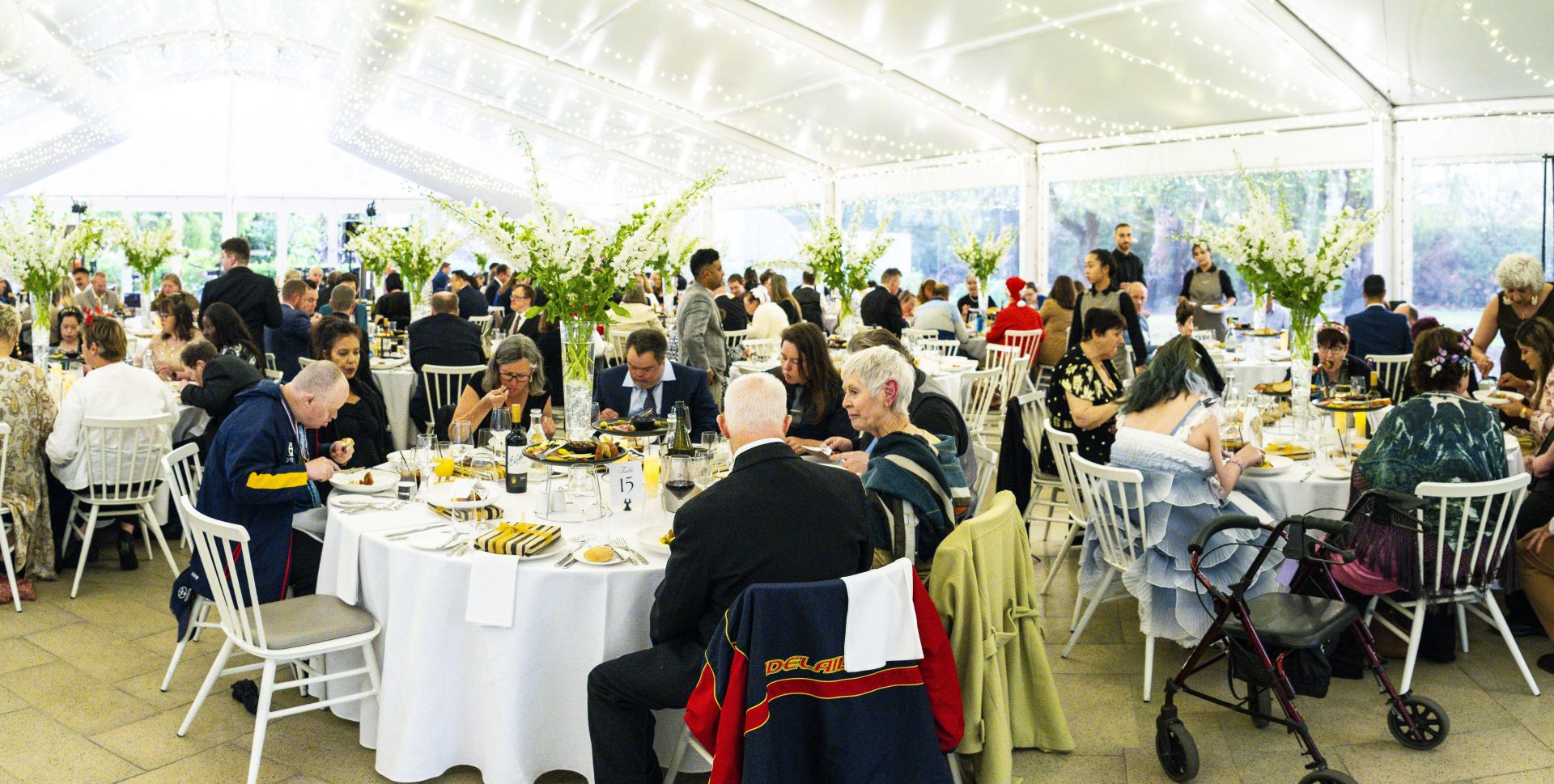 People sitting around round tables in a large marquee with fairy lights above at a gala dinner