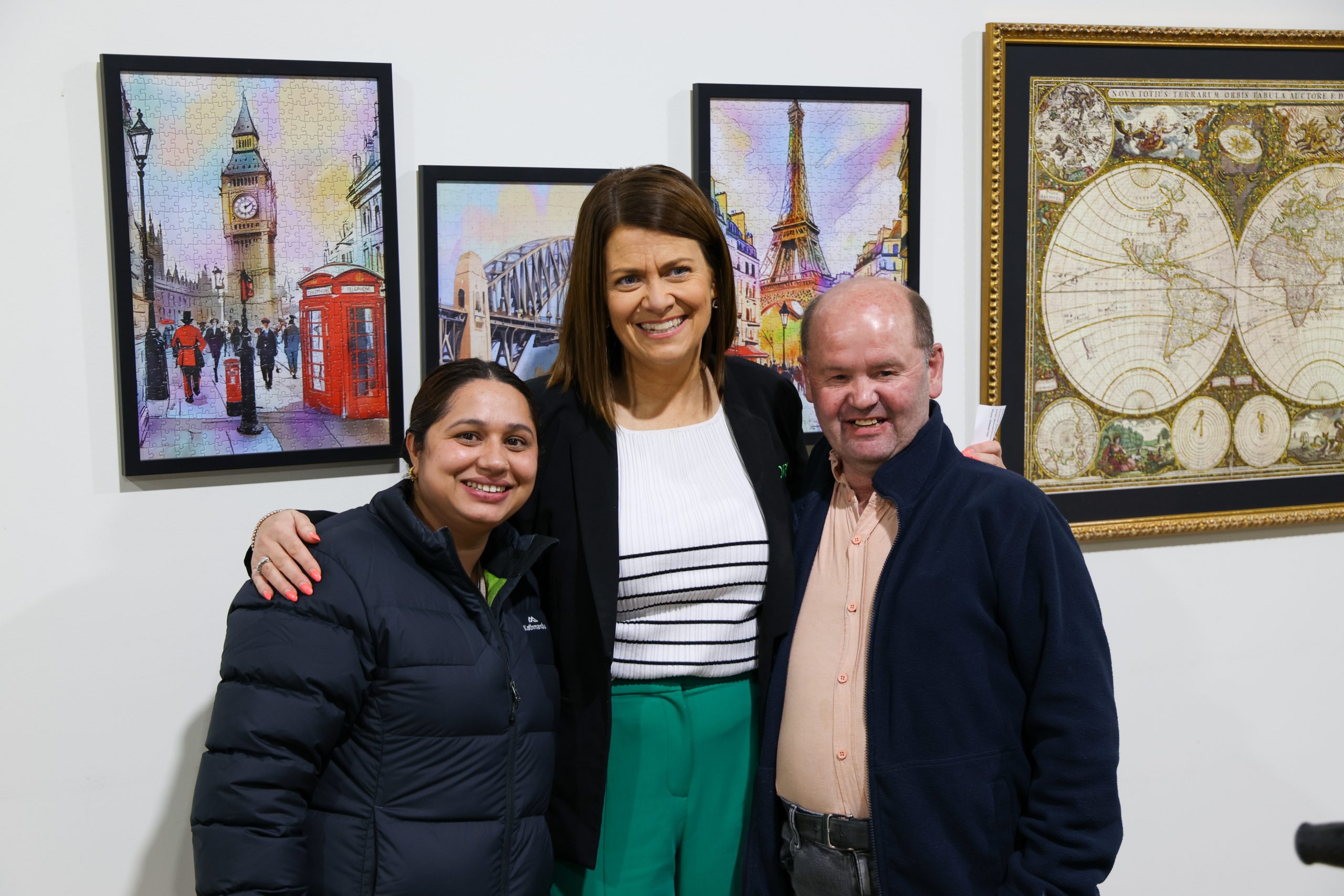 Three people smiling for the camera standing in front of artwork hung on a white wall.